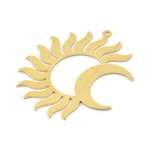 May include: Gold-toned metal pendant featuring a sun and moon design. The sun is stylized with a circular outline and radiating rays. The moon is a crescent shape.