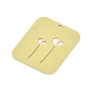 Può includere: Un ciondolo in metallo color oro a forma di rettangolo con due fiori stilizzati ritagliati. Il ciondolo ha un foro nella parte superiore per essere attaccato a una collana o un braccialetto.