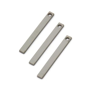 Puede incluir: Tres abalorios de barra de metal plateado con un agujero en la parte superior. Los abalorios son rectangulares y tienen un acabado liso y mate.