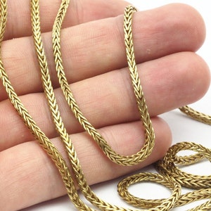 May include: A gold chain necklace with a woven design. The chain is lying on a hand.