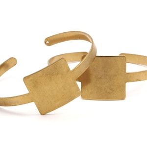 May include: Two gold-toned metal bracelets with square-shaped plates. The plates are blank and ready for personalisation.