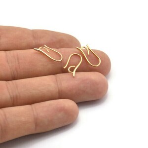 May include: Three gold-toned earring hooks, also known as ear wires, are shown on a hand. The hooks are made of metal and have a simple, elegant design.