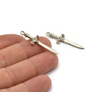 May include: Two silver sword charms with a twisted handle and a pointed tip. The charms are on a white background.