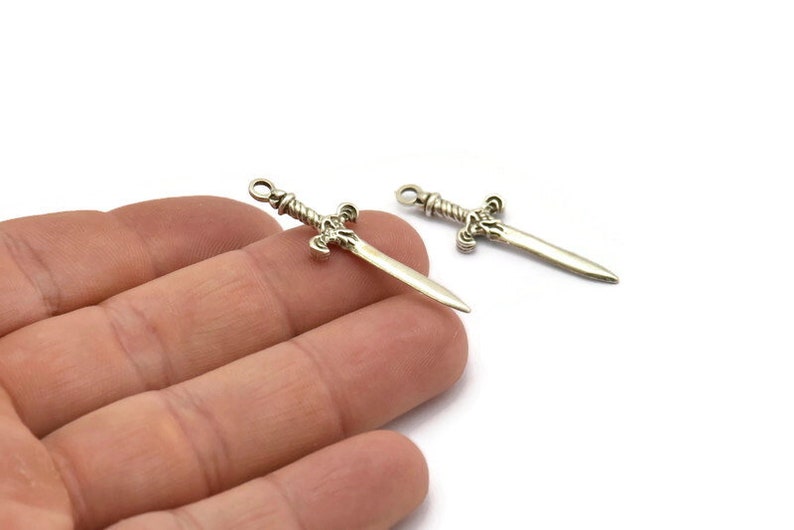 May include: Two silver sword charms with a twisted handle and a pointed tip. The charms are on a white background.