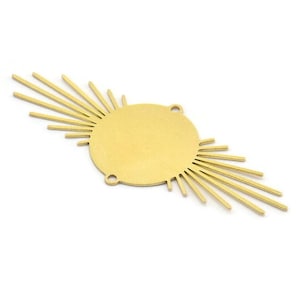 May include: A gold-toned metal sunburst charm with a circular center and radiating points. The charm has two holes for attaching to jewelry.