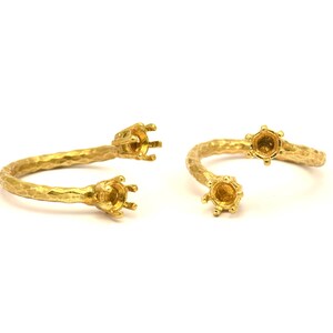 Könnte beinhalten: Zwei goldene Ringe mit offenen Fassungen für Steine. Die Ringe sind texturiert und haben eine gehämmerte Oberfläche.