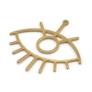 Puede incluir: Encanto de metal dorado en forma de ojo con pestañas. El ojo está delineado y tiene un círculo en el centro.