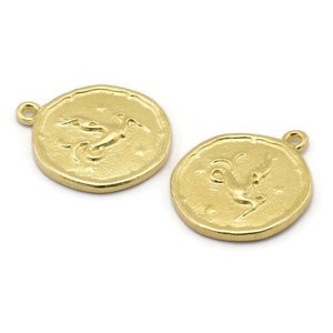 Op de afbeelding: Twee goudkleurige metalen bedels in de vorm van een cirkel met een reli&euml;fdesign van een gestileerde vogel. De bedels hebben een lus aan de bovenkant om aan sieraden te bevestigen.