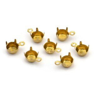 May include: Six gold-toned metal cup-shaped settings with a small loop on the side. These settings are used to hold and secure cabochons or other round stones for jewelry making.