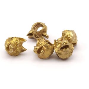 May include: Five gold-colored metal beads, each featuring a detailed wolf head design. The beads are arranged in a cluster on a white background.