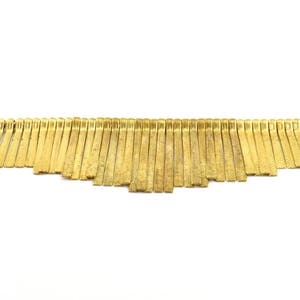 Puede incluir: Una moldura de flecos de metal dorado con una serie de tiras finas, planas y ligeramente texturizadas que cuelgan de una cadena conectada.