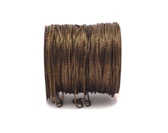 May include: A spool of black and gold metallic cord. The cord is wound tightly around the spool and has a shiny finish.