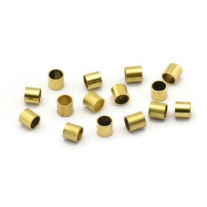 Może przedstawiać: Grupa 15 złotych metalowych koralik&oacute;w do zaciskania, rozrzuconych na białym tle.