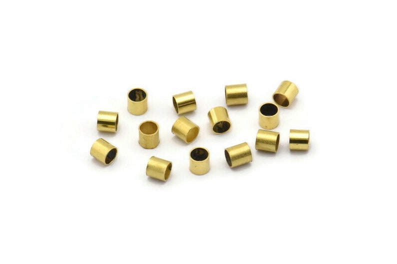 Może przedstawiać: Grupa 15 złotych metalowych koralik&oacute;w do zaciskania, rozrzuconych na białym tle.