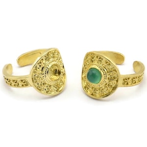 Puede incluir: Dos anillos de oro con diseños intrincados. Un anillo tiene una piedra preciosa verde en el centro. Ambos anillos tienen una parte posterior redondeada y abierta.