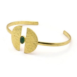 May include: A gold bracelet with two half-circle shapes connected by a thin band. A green gemstone is set in the center of the bracelet.