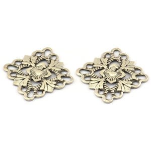 Puede incluir: Dos adornos decorativos de metal plateados con forma cuadrada y diseños florales intrincados.
