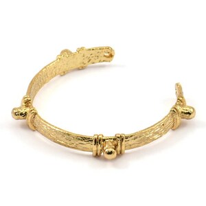 Peut inclure: Un bracelet jonc doré texturé avec des accents décoratifs. Le bracelet est ouvert et possède un fermoir à charnière.