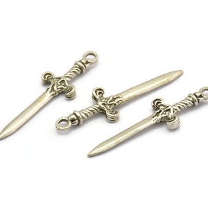 May include: Three silver sword charms with intricate details. The swords have a twisted rope design on the handle and a pointed tip.