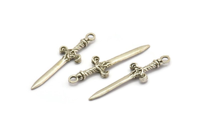 May include: Three silver sword charms with intricate details. The swords have a twisted rope design on the handle and a pointed tip.