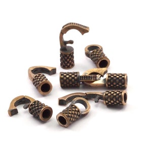 May include: Bronze-colored jewelry clasps with a hook and barrel design. The clasps have a textured, patterned barrel and a curved hook. The clasps are scattered on a white background. These clasps are suitable for necklaces and bracelets.