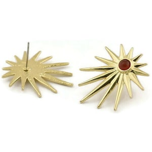 May include: A pair of gold starburst earrings with a red gemstone in the center of each star.