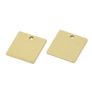 Könnte beinhalten: Zwei quadratische, goldfarbene Metallanhänger mit einem kleinen Loch oben zum Auffädeln. Die Anhänger sind blank und glatt, ideal für die Schmuckherstellung oder andere Bastelprojekte. Die Anhänger werden vor weißem Hintergrund gezeigt.