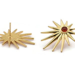 May include: A pair of gold starburst earrings with a red gemstone in the center of each star.