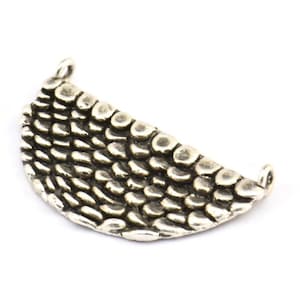 May include: Silver pendant with a textured, half-circle design resembling scales. The pendant has two loops for attaching a chain or cord.