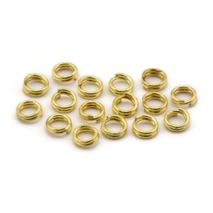 May include: A group of 15 gold jump rings, each with a double loop design. The rings are scattered on a white surface.