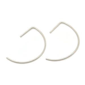 May include: A pair of silver-colored, minimalist hoop earrings. Each earring features a curved, semi-circular design with a straight, angular top. The earrings are presented against a plain white background, highlighting their sleek, modern aesthetic.