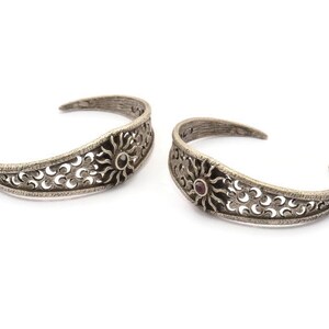 May include: Two silver bracelets with intricate filigree designs and a small red gemstone in the center of each.