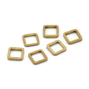 Puede incluir: Seis pequeños anillos cuadrados de latón con esquinas redondeadas están dispersos sobre un fondo blanco. Los anillos tienen un acabado mate ligeramente envejecido, lo que sugiere una estética vintage o antigua. Probablemente sean hallazgos de joyería o suministros de artesanía.
