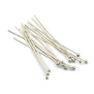 Könnte beinhalten: Eine Gruppe von silbernen Stecknadeln mit runden Köpfen. Die Nadeln sind in einem zufälligen Muster auf einem weißen Hintergrund angeordnet.