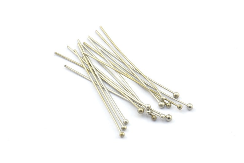 May include: A group of silver head pins with round heads. The pins are arranged in a random pattern on a white background.