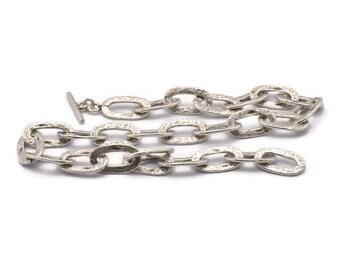 May include: A silver chain necklace with a textured, hammered finish. The chain is made of oval links and has a t-bar clasp.