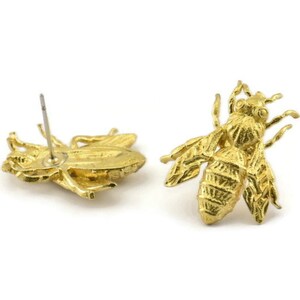 May include: A pair of gold bee stud earrings. The earrings are made of metal and have a detailed bee design.