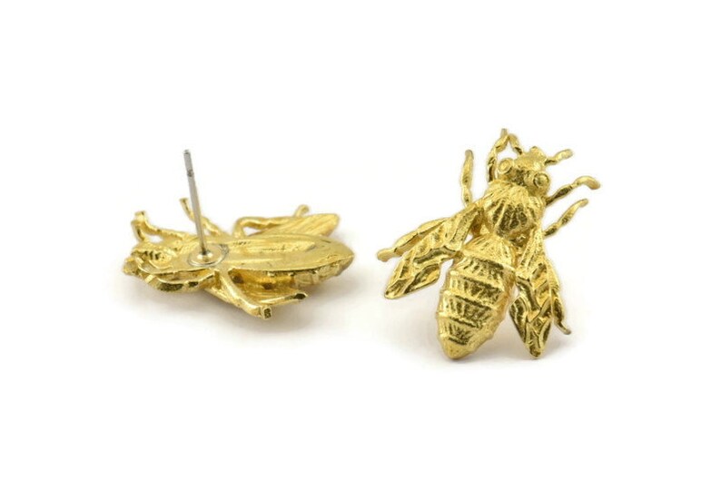 May include: A pair of gold bee stud earrings. The earrings are made of metal and have a detailed bee design.