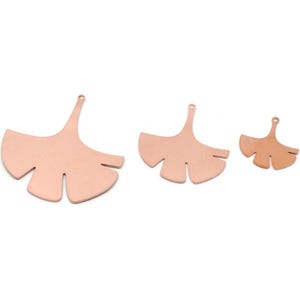 May include: Three copper-coloured Ginkgo leaf charms in varying sizes, each with a small hole for hanging. The leaves are flat and have a smooth surface, ideal for jewellery making or other craft projects.