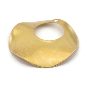 May include: A gold-toned metal pendant with a wavy, organic shape and a circular hole in the center.