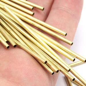 May include: A close-up of a hand holding a bundle of thin, gold-colored brass tubes. The tubes are all the same size and are arranged in a random pattern.