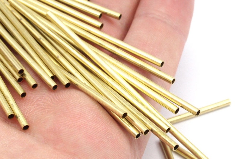 May include: A close-up of a hand holding a bundle of thin, gold-colored brass tubes. The tubes are all the same size and are arranged in a random pattern.