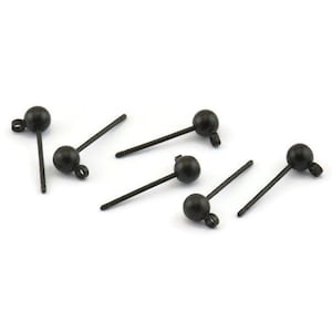 Könnte beinhalten: Sechs schwarze Ohrstecker mit kugelförmigem Aufsatz und einem Stift zum Einsetzen. Die Ohrringe sind auf weißem Hintergrund verstreut. Die Ohrringe haben eine kleine Schlaufe am Ende des Stifts.