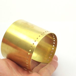 K&ouml;nnte beinhalten: Ein goldfarbenes Metall-Armband mit einer Reihe kleiner L&ouml;cher am Rand.