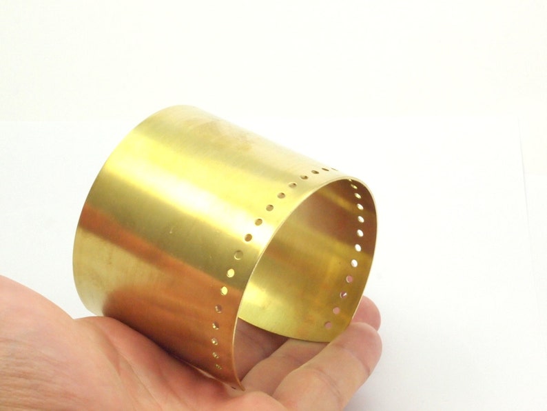 K&ouml;nnte beinhalten: Ein goldfarbenes Metall-Armband mit einer Reihe kleiner L&ouml;cher am Rand.