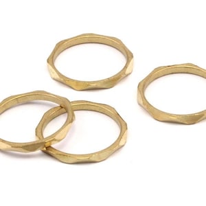 Puede incluir: Cuatro anillos de metal de color dorado con un diseño facetado. Los anillos están apilados uno encima del otro.