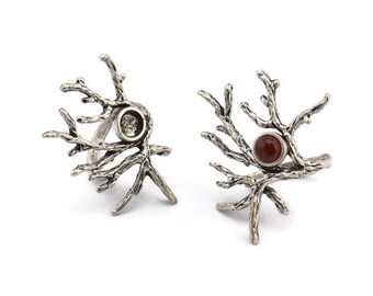 Puede incluir: Dos anillos de plata con forma de ramas con piedras preciosas. Un anillo tiene una piedra preciosa transparente y el otro tiene una piedra preciosa roja.