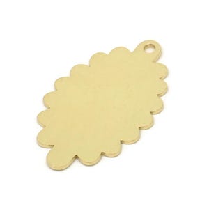 Könnte beinhalten: Goldfarbener Metallanhänger mit einem gewellten Rand in Form eines Ovals. Der Anhänger hat ein kleines Loch oben zum Anbringen an einer Halskette oder einem Armband.