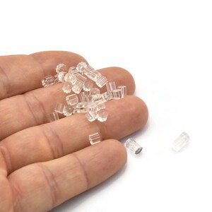 May include: A pile of clear plastic earplugs in a hand. The earplugs are small and cylindrical.
