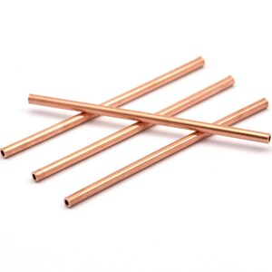 May include: Four copper coloured metal tubes, each with a hollow centre, are stacked on top of each other.